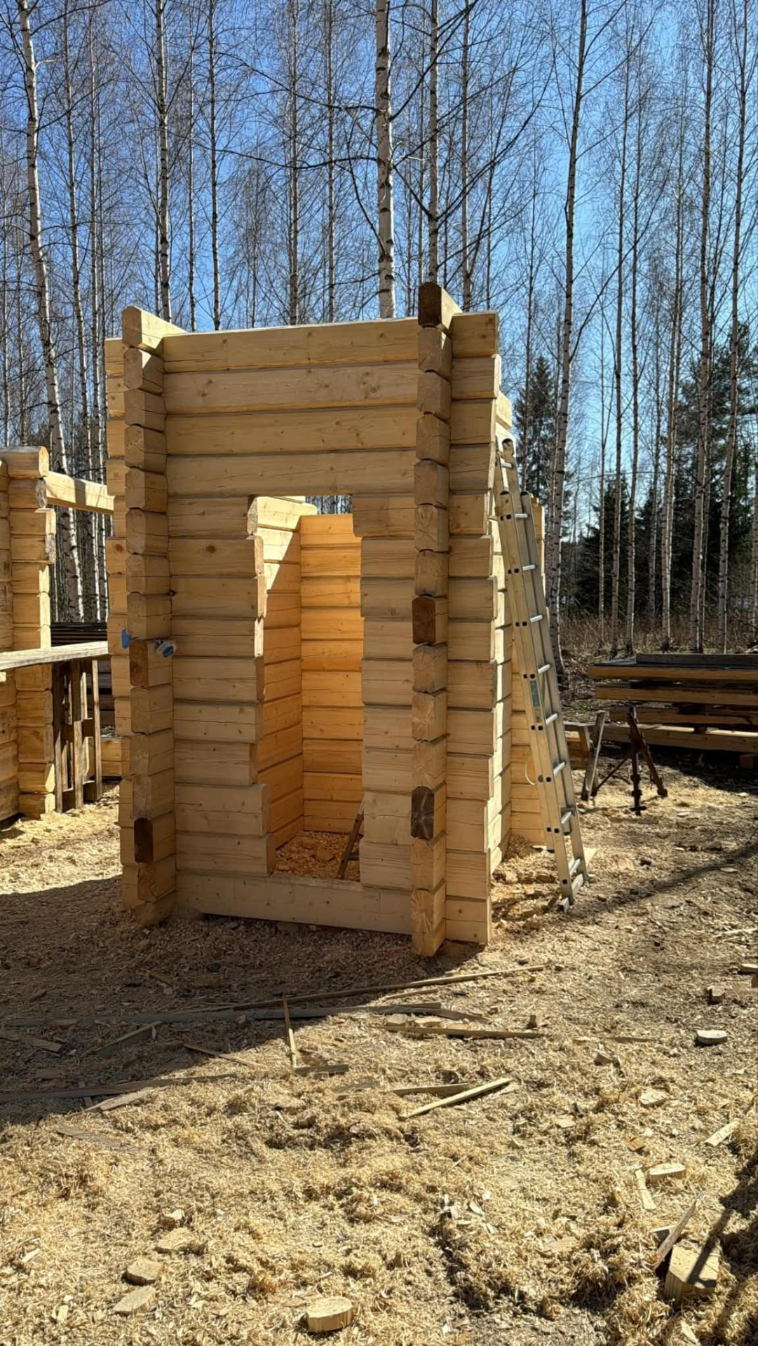 Pieni hirsikehikko metsäisellä työmaalla traktorin vieressä.